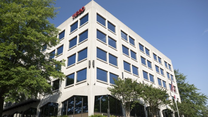 Exterior view of five-story white modern office building with large windows, landscaping, and clear blue sky