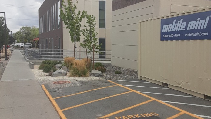 Exterior view of modern medical building facade with tan and brown metal siding along pedestrian pathway and parking area