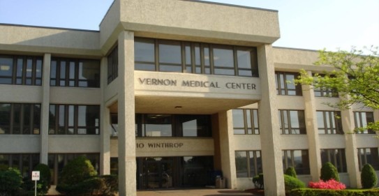 Exterior view of multi-story tan brick medical building with signage, windows, and landscaped grounds.