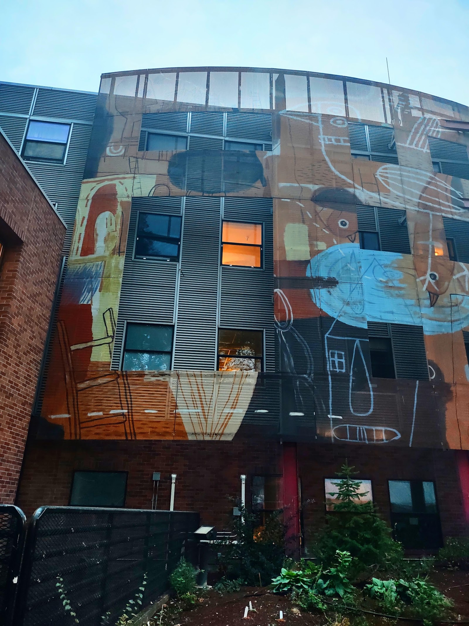 Building exterior with colorful illustrated mural art featuring figures and geometric shapes on brick facade