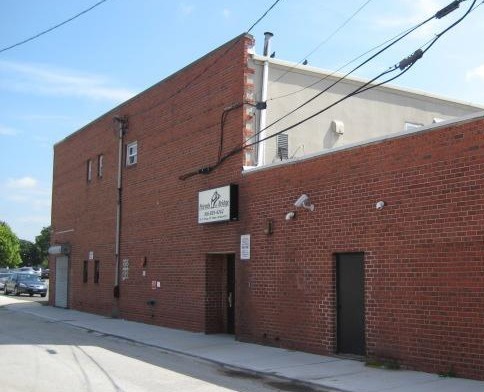 Red brick building exterior with parked vehicles, utility lines, and facility side entrance area