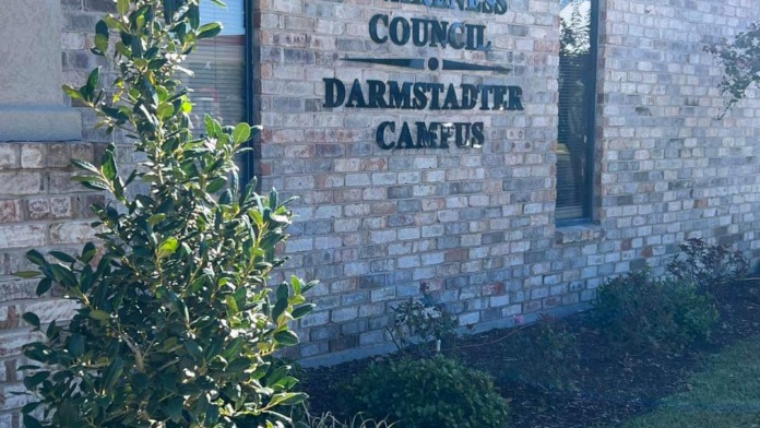 Exterior brick wall showing ADAC facility signage with ornamental landscaping, shrubs, and flowering plants