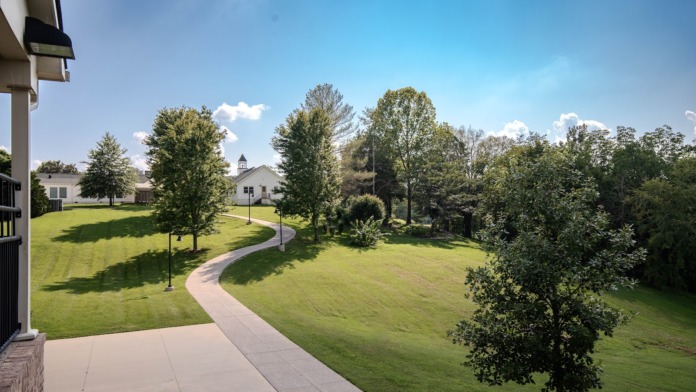 Exterior view of manicured campus grounds with curved walkway, mature trees, and multiple facility buildings