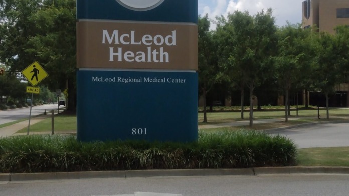 Outdoor pedestrian pathway with blue McLeod Health building 3 directional sign and tree-lined landscape area