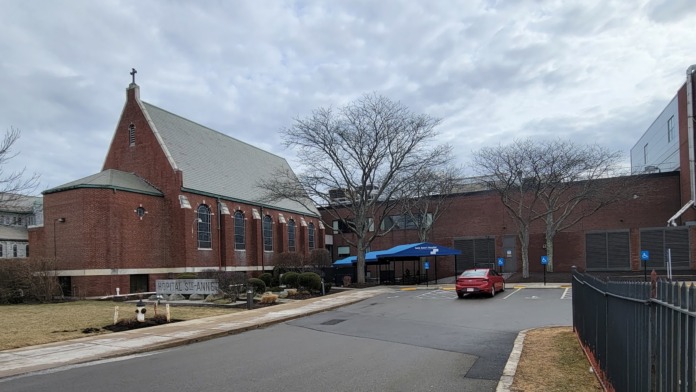 Exterior brick chapel with distinctive steeple and pointed roof, modern facility structures visible adjacent to historic building