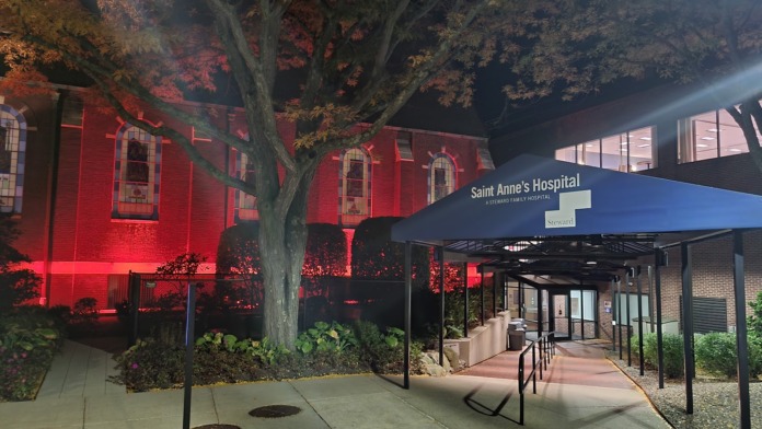 Night-time exterior of red brick chapel building with red lighting, large tree and modern entrance canopy visible