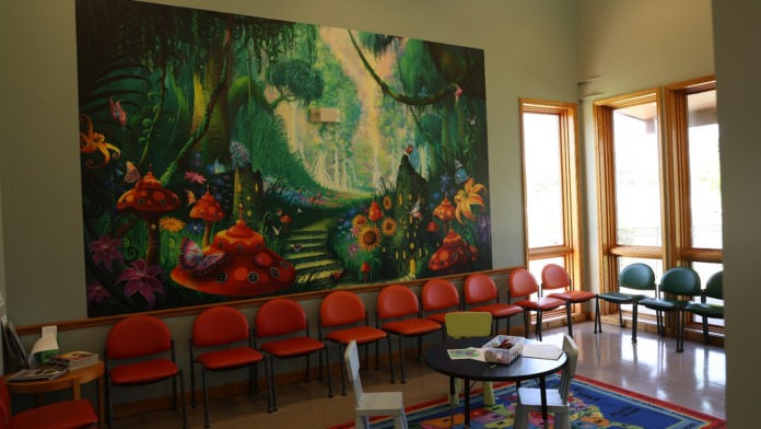 Interior recreation space with colorful whimsical mural featuring mushroom houses, bright seating furniture, and natural lighting from large windows
