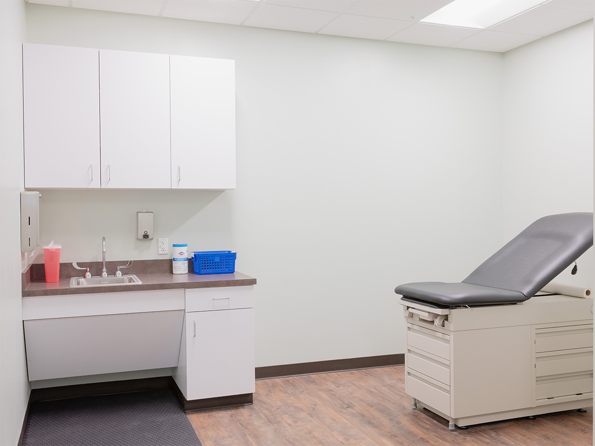 Interior clinical space with examination table, white cabinetry, sink, and medical equipment storage