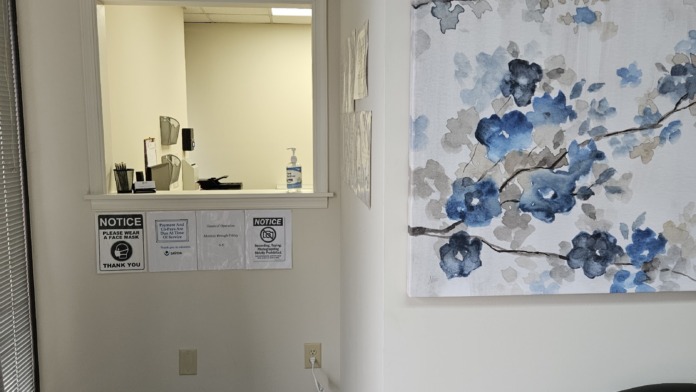 Interior office with reception window, wall clock, floral artwork, wooden flooring, and professional furnishings.