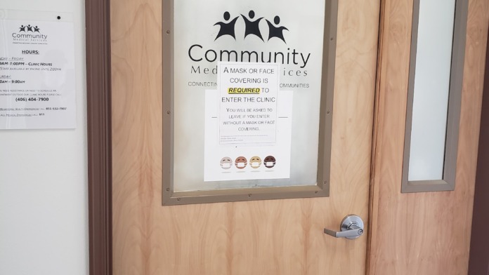 Interior door with frosted glass panel displaying Community Medical Services logo and mask requirement notice posted