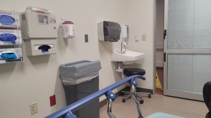 Interior medical room with wall-mounted monitors, sink, medical equipment, and supply storage