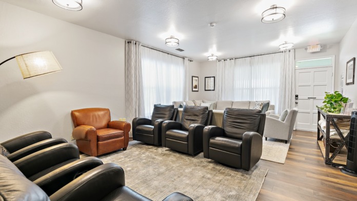 Interior common area with leather recliners, sofas, white sheer curtains, modern lighting fixtures, and exit signage
