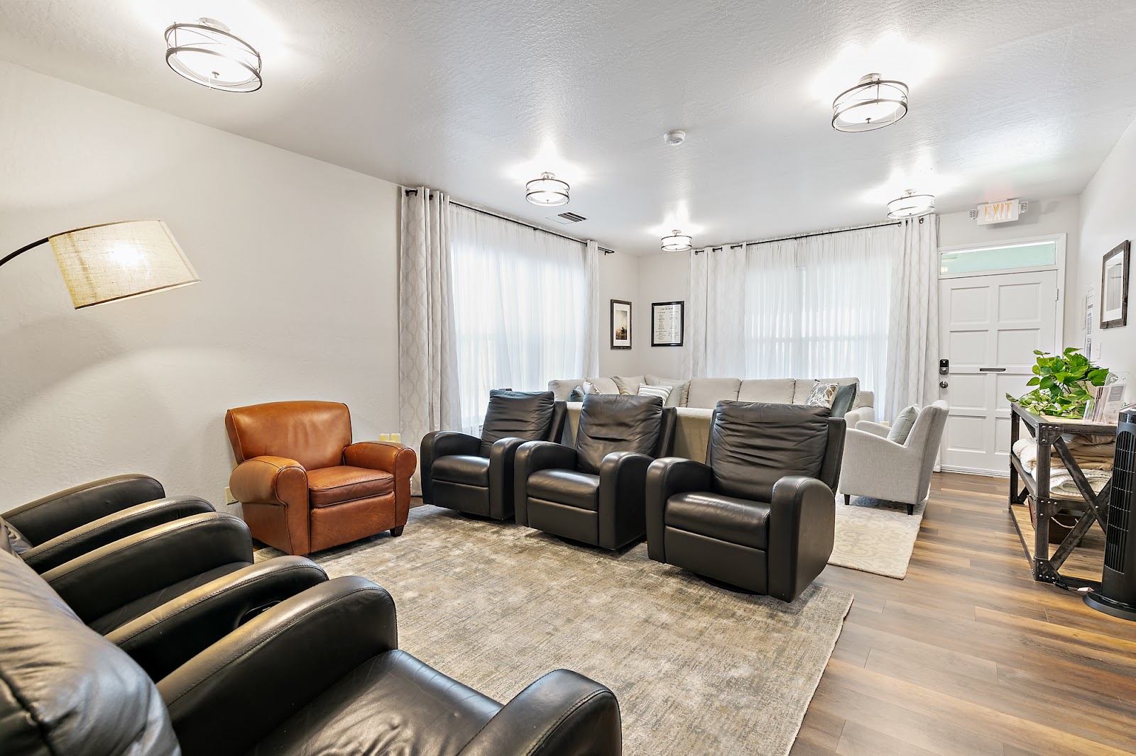Interior common area with leather recliners, sofas, white sheer curtains, modern lighting fixtures, and exit signage