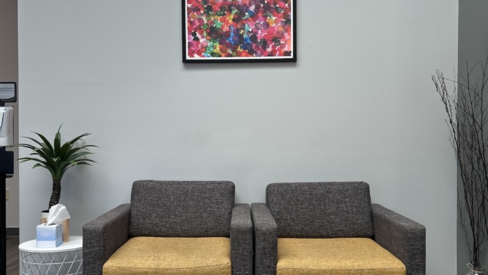 Interior lounge with gray and yellow upholstered armchairs, colorful abstract wall art, small side table, and decorative plants