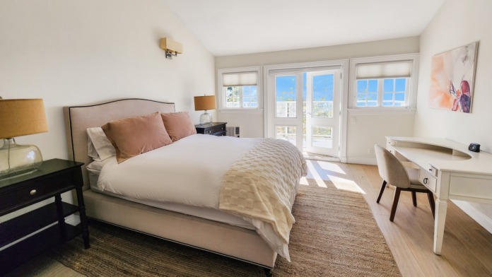Interior patient bedroom with queen bed, desk, sliding glass doors to ocean-view patio, and natural lighting