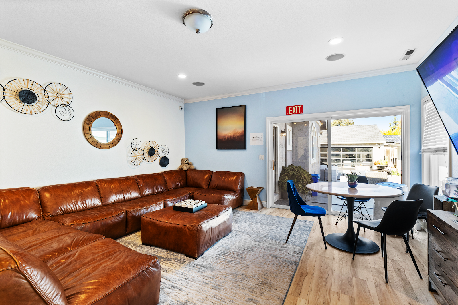 Interior common room with brown leather sectional sofa, dining table, blue accent walls, and decorative art