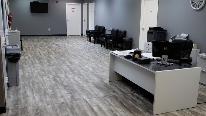 Interior common area with blue-gray walls, reception desk, seating, wall-mounted television, and drop ceiling lighting
