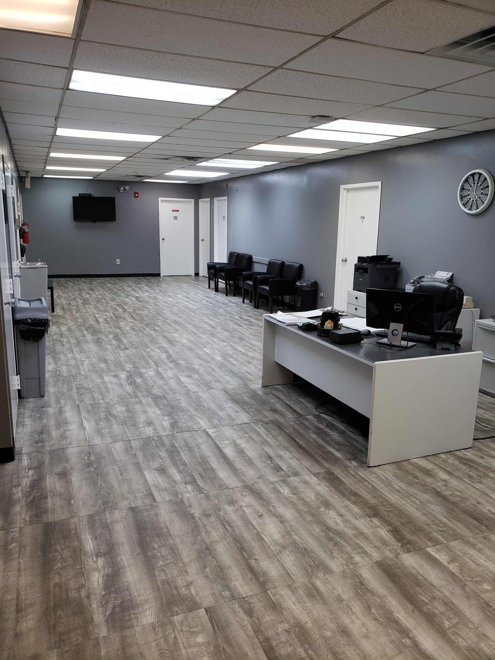 Interior common area with blue-gray walls, reception desk, seating, wall-mounted television, and drop ceiling lighting