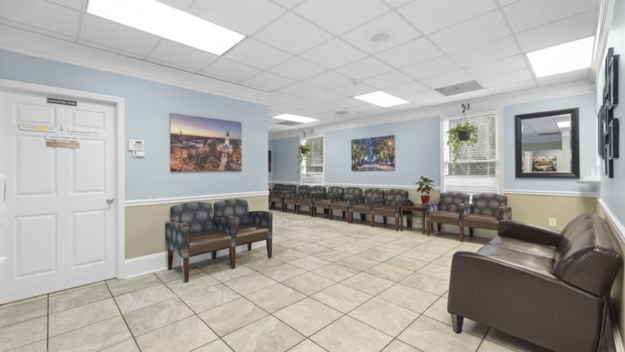 Interior common area with multiple leather chairs and sofas, light blue walls, cream wainscoting, tile flooring, and framed landscape artwork