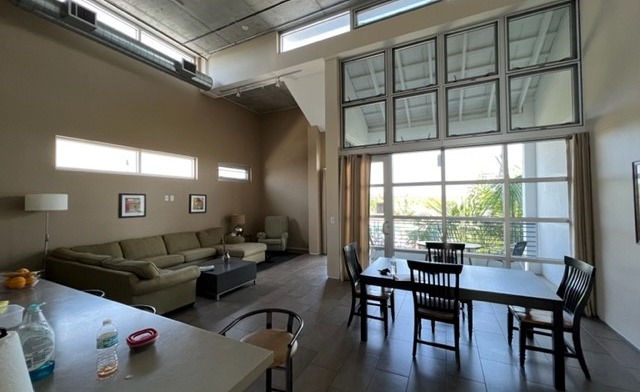 Interior common room with green sofa, skylight, wooden dining table and chairs, glass doors leading to patio area.