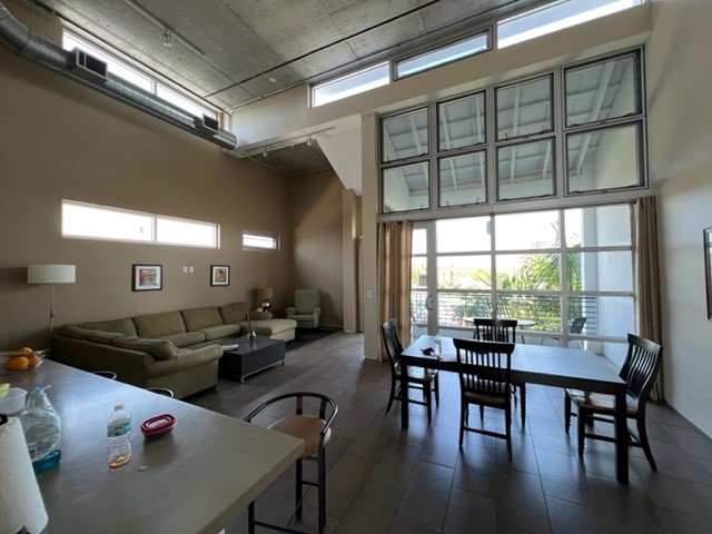 Interior common room with green sofa, skylight, wooden dining table and chairs, glass doors leading to patio area.