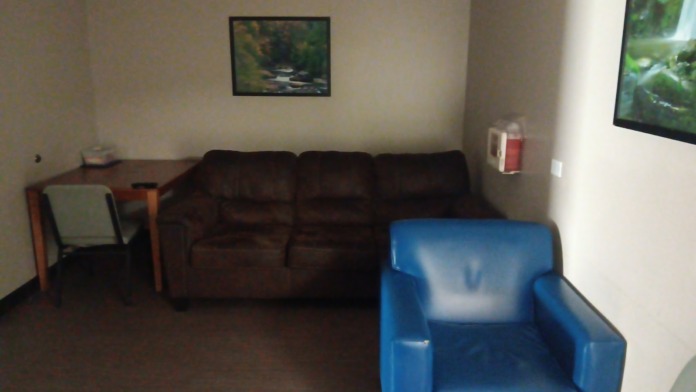 Interior lounge space with brown sofa, blue chair, desk, and wall-mounted framed artwork and television