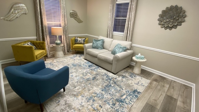 Interior lounge space with yellow and blue modern chairs, cream sofa, patterned rug, and windows with blinds