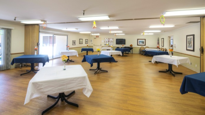 Interior large multipurpose room with multiple dining tables, wooden flooring, decorative fabric arrangements, and side serving areas