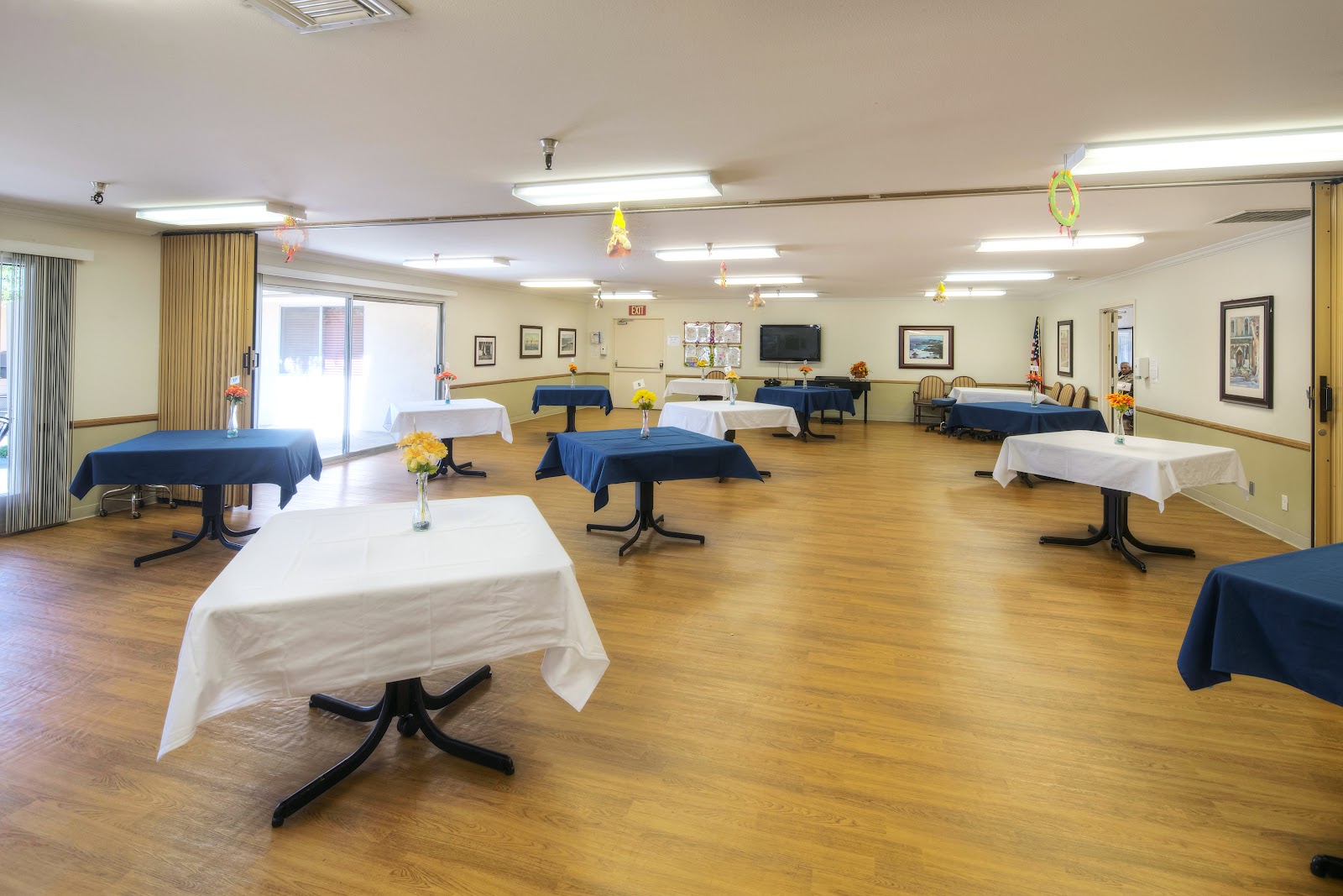 Interior large multipurpose room with multiple dining tables, wooden flooring, decorative fabric arrangements, and side serving areas