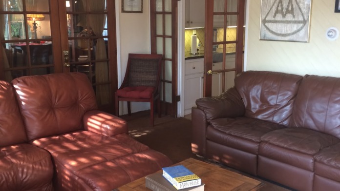 Interior living room with burgundy leather seating, wooden furnishings, glass-fronted cabinets, and facility signage