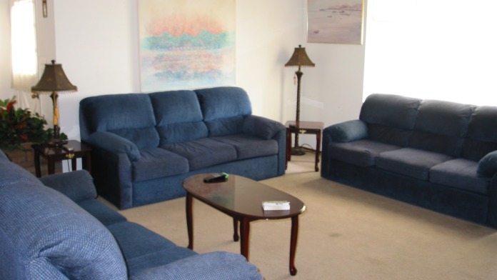 Interior common area with three upholstered sofas arranged around coffee table, artwork on walls, and natural lighting from windows