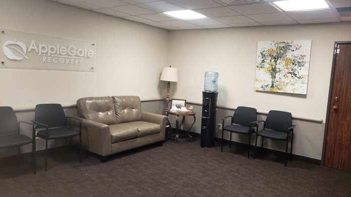 Interior lounge with AppleGate Recovery branding, leather furniture, black chairs, and skylight ceiling panels.