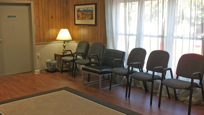 Interior common area with wooden walls, comfortable seating chairs, table with lamp, large windows with curtains, and artwork on walls