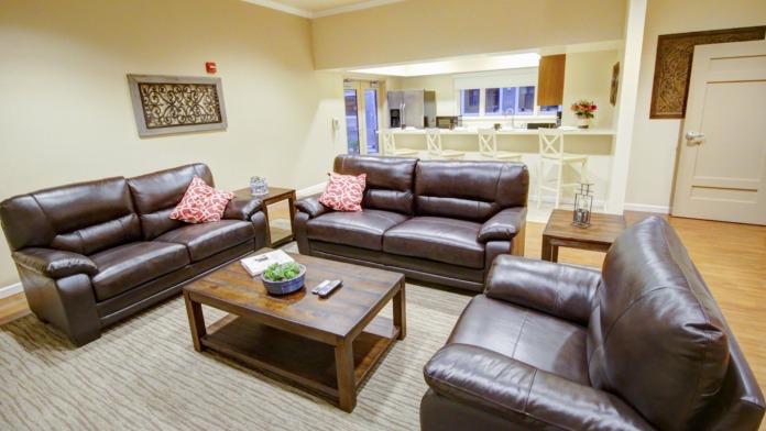 Interior lounge area with brown leather couches, wooden coffee table, decorative wall art, check-in counter, and large windows