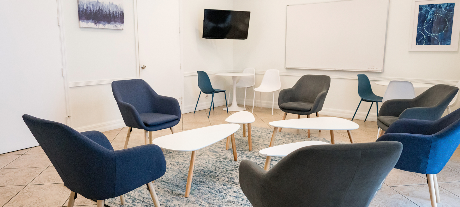 Interior community lounge with multiple comfortable chairs, tables, television, and natural lighting from large windows
