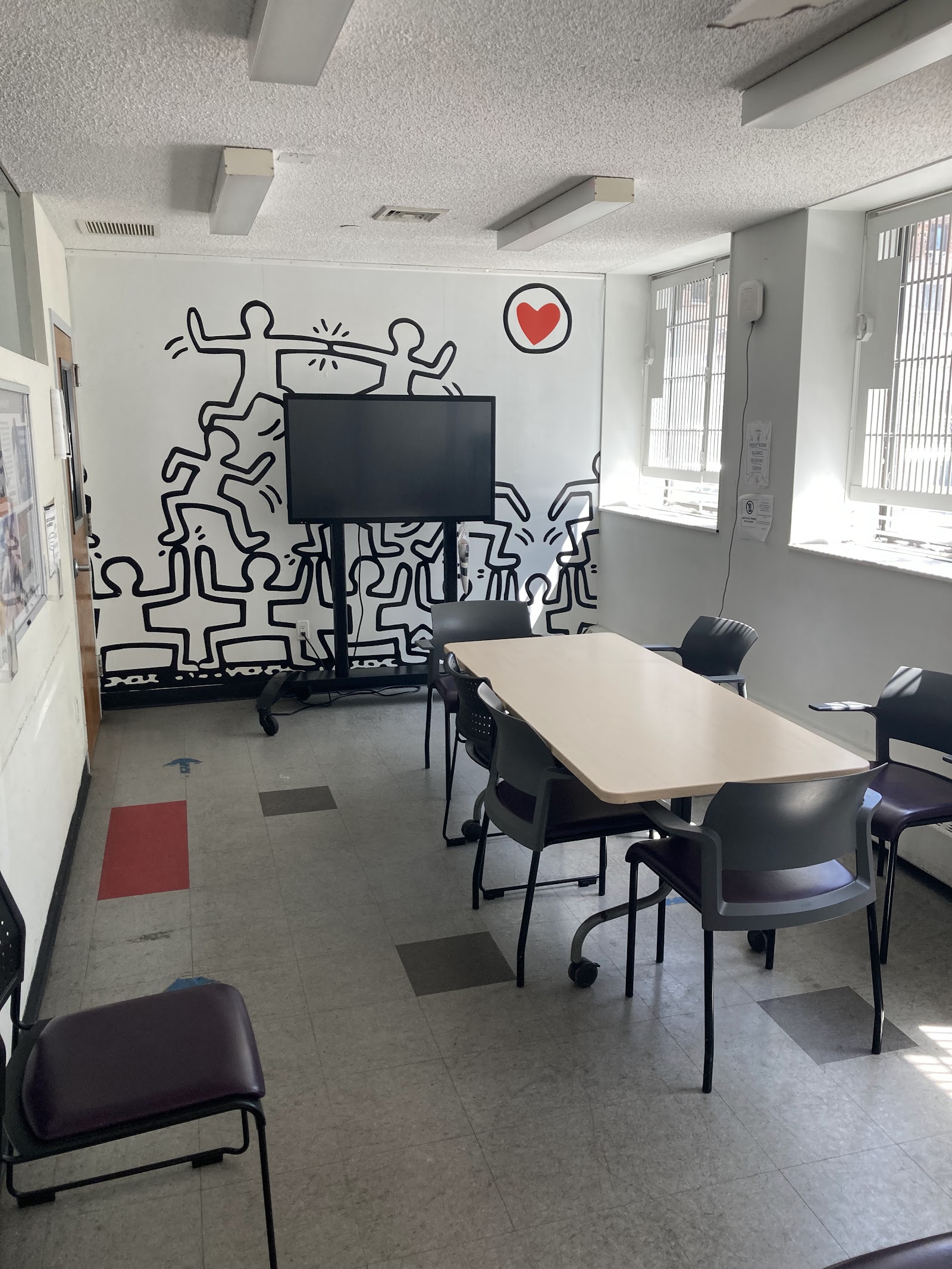 Interior community space with mural artwork, conference table, television, and seating for group activities.