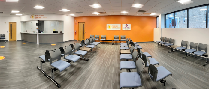 Interior reception space with seating arranged in rows, orange accent wall, service desk, and windows overlooking street