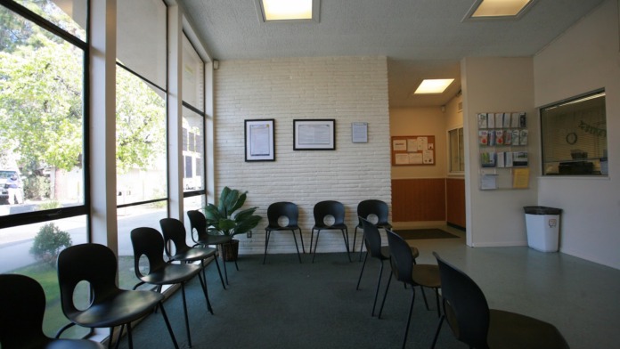 Interior waiting area with black chairs, large windows with natural light, brick walls, and potted plant