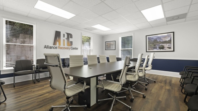 Interior conference room featuring long black table, office chairs, Alliance Recovery Center logo, and landscape artwork