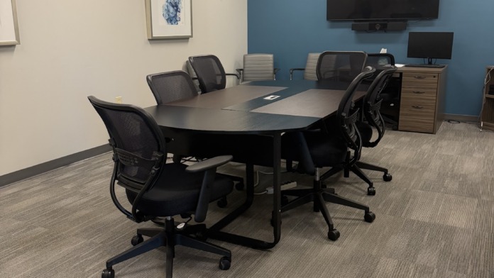 Interior conference room with oval black table, mesh office chairs, blue accent wall, mounted TV, and framed artwork