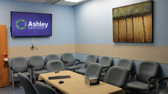 Interior meeting room with Ashley Addiction Treatment logo on screen, upholstered seating, and light wood conference table.