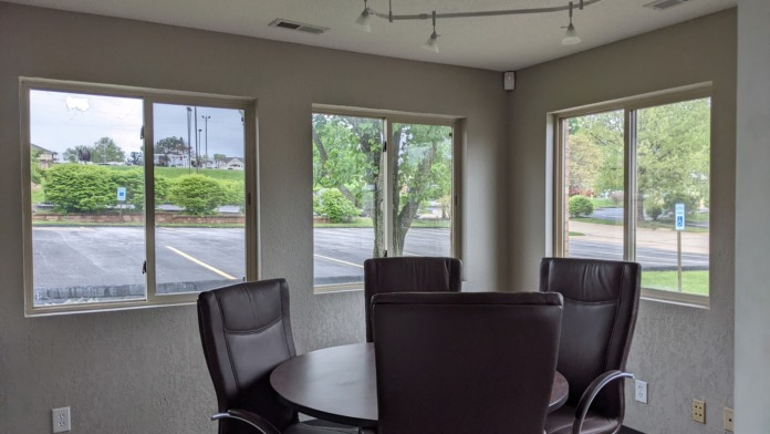 Interior meeting space with round dark table, four black leather office chairs, and windows overlooking parking area and grounds.