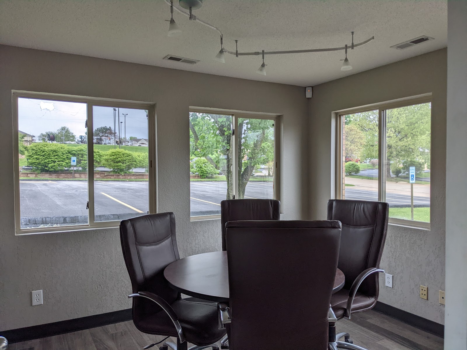 Interior meeting space with round dark table, four black leather office chairs, and windows overlooking parking area and grounds.