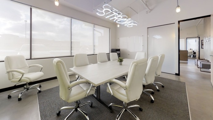 Interior conference room with white conference table, leather chairs, neon signage, and large windows