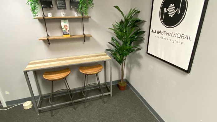 Interior small meeting room with dark carpet, wall signage, high-top table with stools, and minimalist modern design