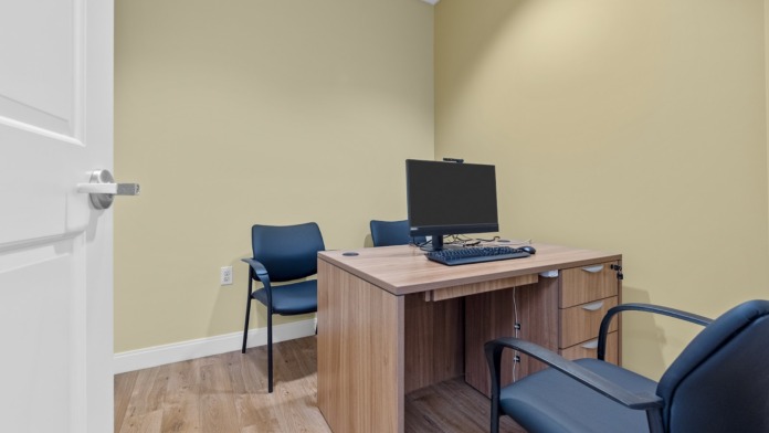Interior consultation room with wooden desk, blue office chairs, yellow-green wall treatment, and glass partition window