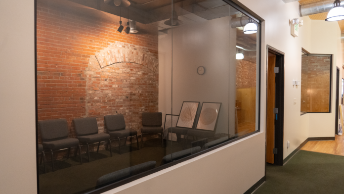 Glass-partitioned interior room with seating, hallway access, and tan walls