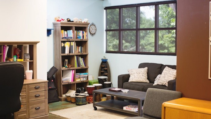 Interior multipurpose space with varied seating options including armchairs and sofas, decorative artwork, large windows with natural light, and floor lamps