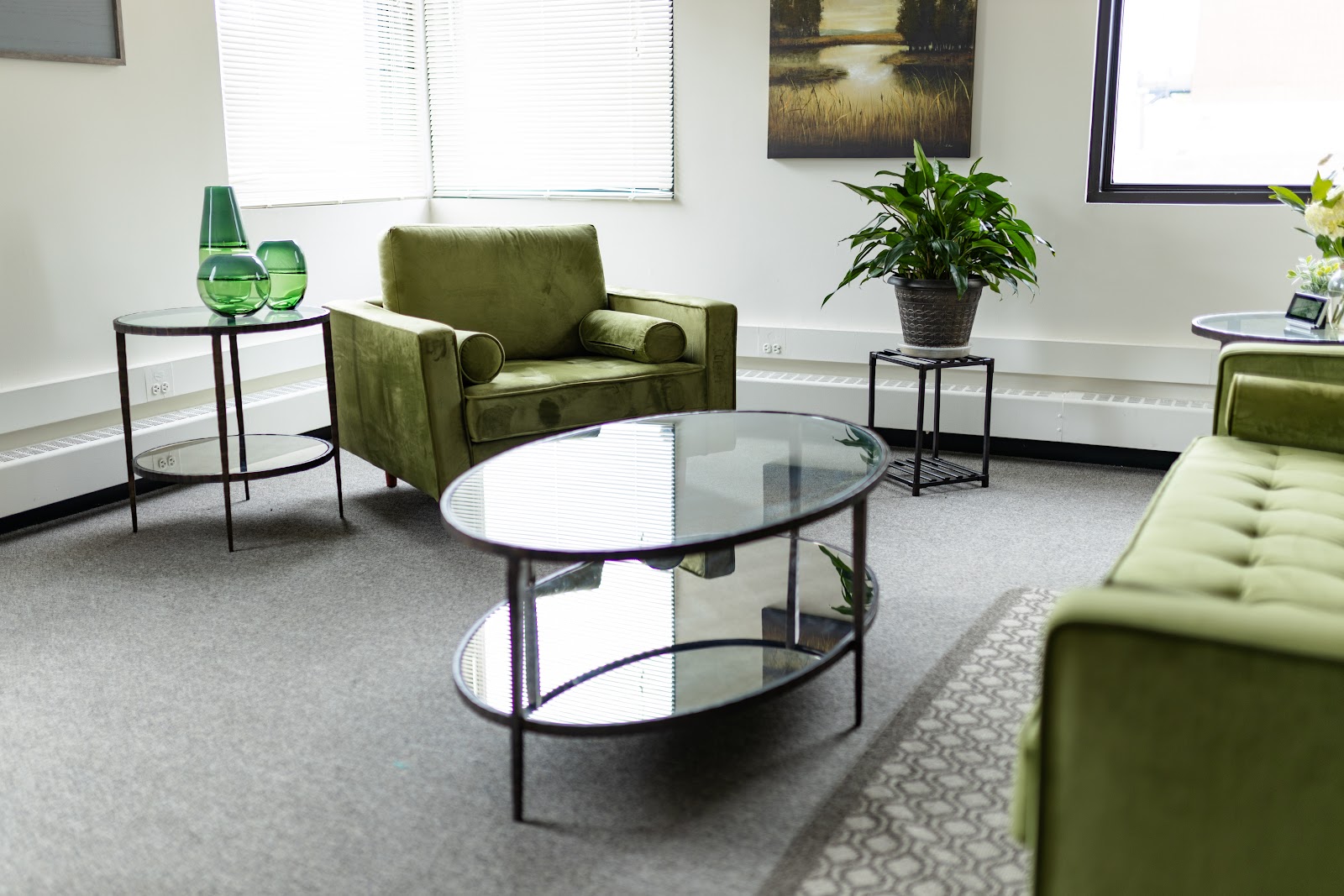 Interior lounge area with green armchairs, round glass table, potted plants, and professional furnishings