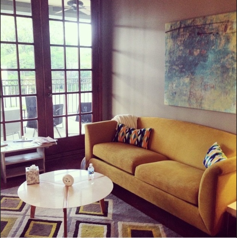 Interior seating area with mustard-yellow sofa, round table, large window, artwork, and contemporary furnishings
